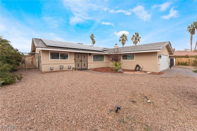 ranch-style home with a gate, roof mounted solar panels, fence, an attached garage, and brick siding