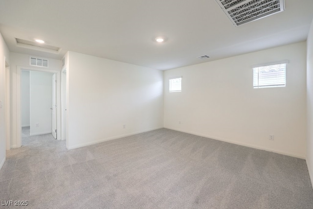 carpeted spare room featuring visible vents, baseboards, and attic access