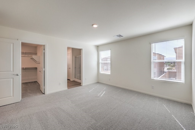 unfurnished bedroom featuring visible vents, light carpet, a walk in closet, a closet, and baseboards