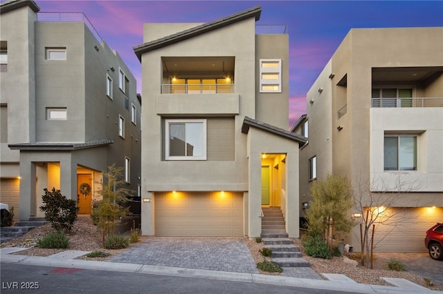 contemporary home featuring stucco siding, an attached garage, decorative driveway, and a balcony