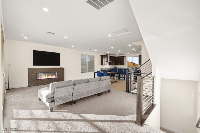 living area with recessed lighting, visible vents, a glass covered fireplace, and stairs