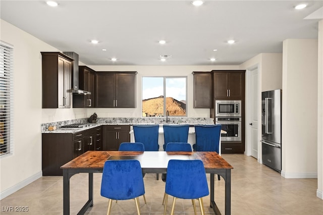 kitchen featuring recessed lighting, stainless steel appliances, dark brown cabinetry, and wall chimney range hood