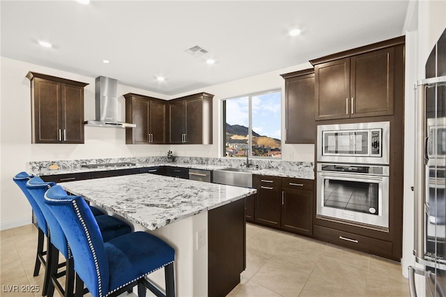 kitchen with visible vents, a kitchen island, a sink, appliances with stainless steel finishes, and wall chimney exhaust hood