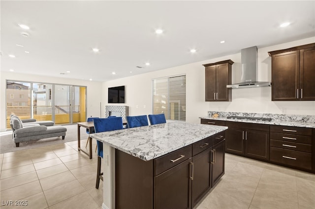 kitchen with a kitchen island, wall chimney range hood, stainless steel gas cooktop, open floor plan, and a kitchen breakfast bar