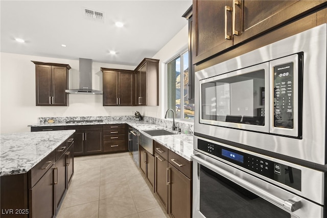 kitchen with visible vents, a sink, dark brown cabinetry, appliances with stainless steel finishes, and wall chimney range hood