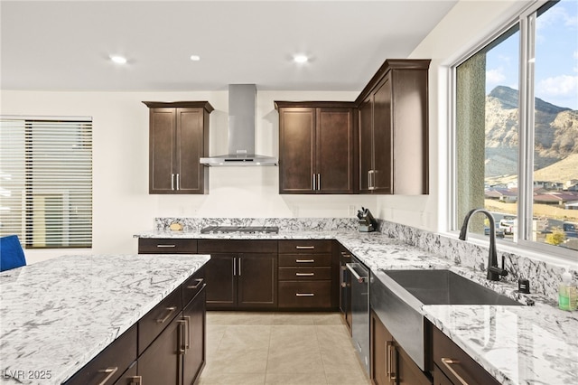 kitchen with light stone countertops, a sink, dark brown cabinets, appliances with stainless steel finishes, and wall chimney range hood