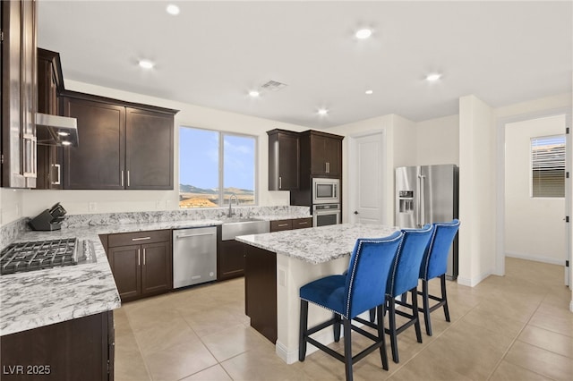 kitchen featuring visible vents, stainless steel appliances, dark brown cabinets, under cabinet range hood, and a center island