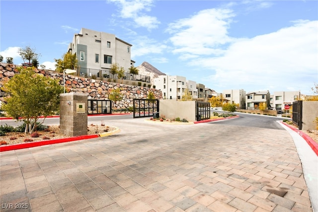 view of road featuring a gate, curbs, a residential view, and a gated entry