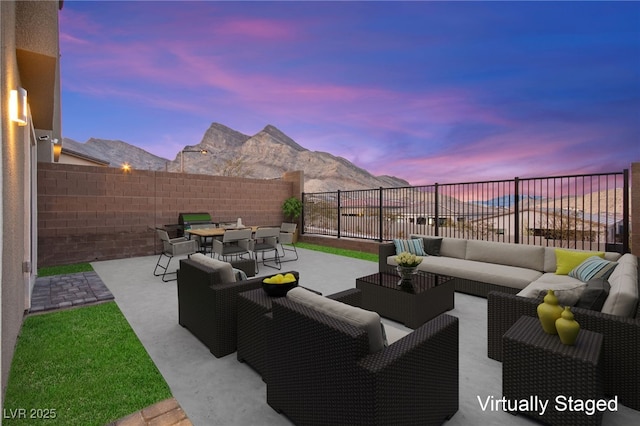 patio terrace at dusk with outdoor dining space, an outdoor living space, a fenced backyard, and a mountain view