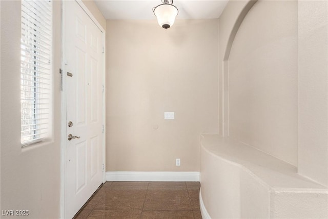 corridor with tile patterned floors, arched walkways, and baseboards