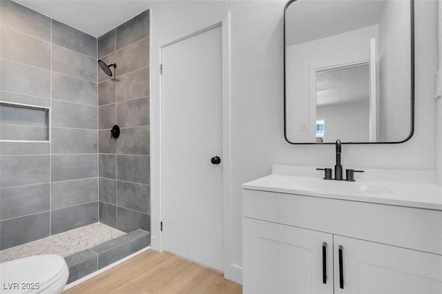 full bath featuring toilet, tiled shower, vanity, and wood finished floors