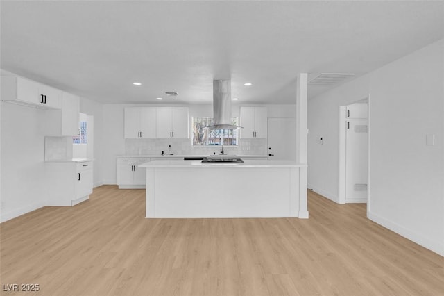 kitchen with light wood finished floors, decorative backsplash, white cabinets, and island exhaust hood