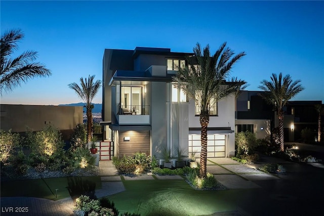 contemporary house featuring stairs, stucco siding, driveway, a balcony, and an attached garage