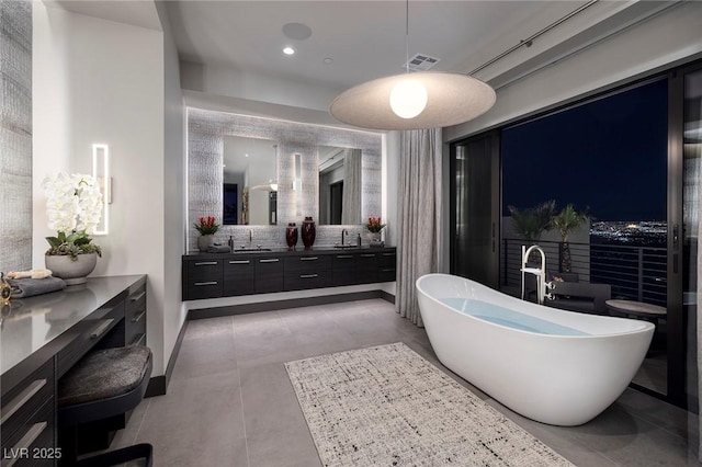 full bathroom with a freestanding bath, double vanity, tile patterned flooring, and a sink