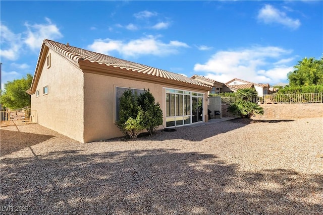 rear view of property with stucco siding, a tile roof, and fence