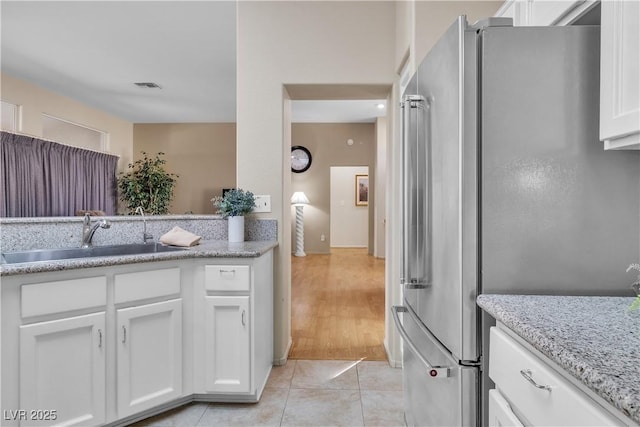 kitchen featuring light tile patterned floors, visible vents, freestanding refrigerator, a sink, and white cabinets