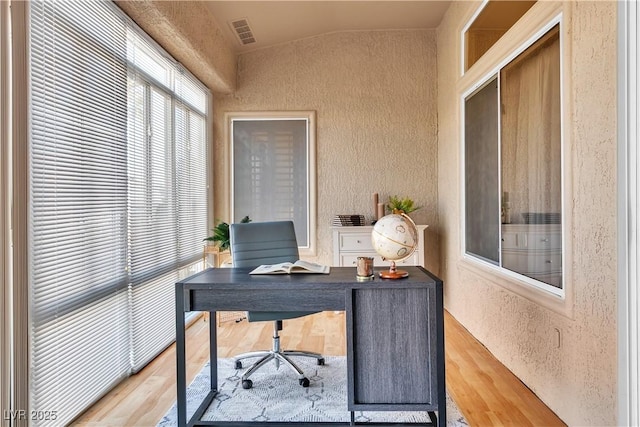 office with visible vents, wood finished floors, and a textured wall