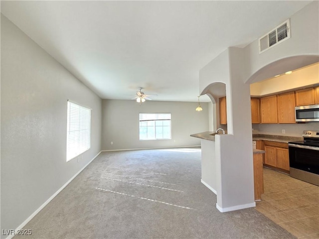 kitchen featuring visible vents, stainless steel appliances, brown cabinetry, baseboards, and light colored carpet