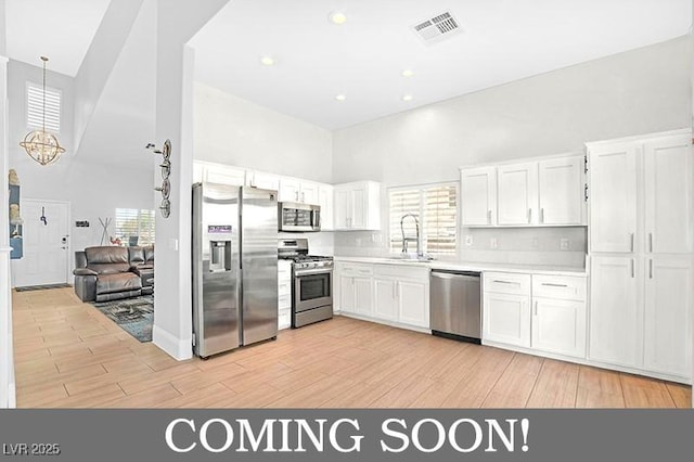 kitchen featuring visible vents, a sink, a towering ceiling, appliances with stainless steel finishes, and white cabinetry