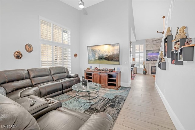 living area featuring ceiling fan, a high ceiling, and baseboards