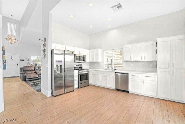 kitchen featuring a sink, stainless steel appliances, a towering ceiling, and white cabinets