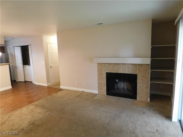 unfurnished living room with a tiled fireplace, wood finished floors, baseboards, and visible vents