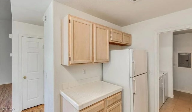 kitchen featuring light brown cabinets, tile countertops, electric panel, freestanding refrigerator, and washer and dryer