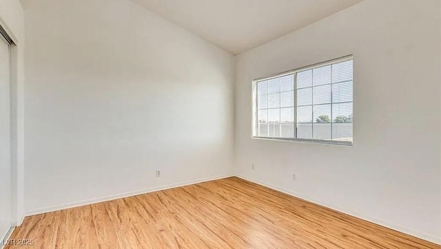 empty room featuring baseboards, vaulted ceiling, and light wood finished floors