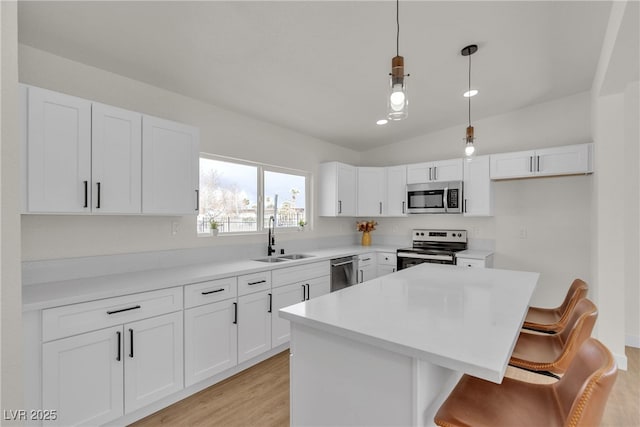 kitchen with a kitchen island, a breakfast bar, appliances with stainless steel finishes, white cabinetry, and a sink