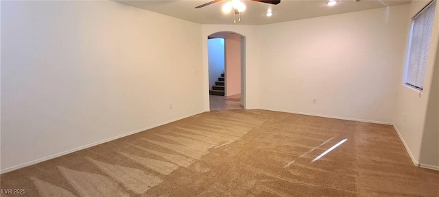 spare room featuring arched walkways, carpet flooring, baseboards, and ceiling fan