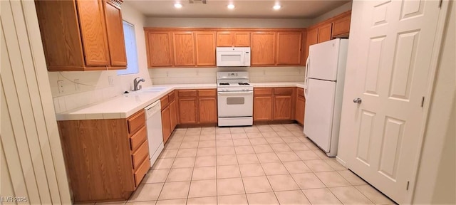 kitchen featuring light countertops, recessed lighting, brown cabinetry, white appliances, and a sink