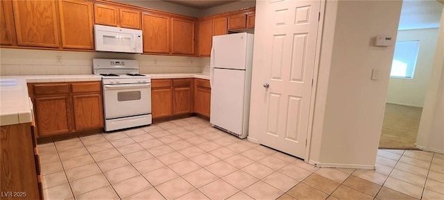 kitchen with light tile patterned floors, brown cabinets, white appliances, and tile counters