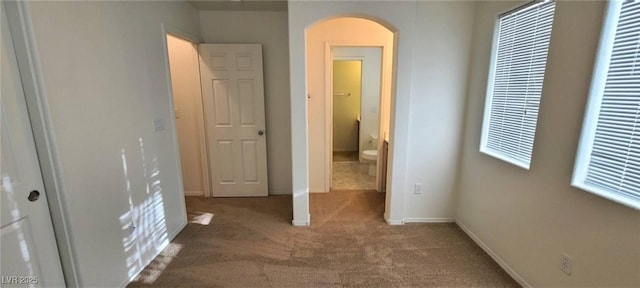 unfurnished bedroom with baseboards, arched walkways, and carpet floors