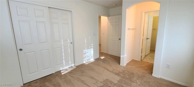 unfurnished bedroom featuring a closet, arched walkways, baseboards, and carpet flooring