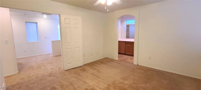 empty room with visible vents, ceiling fan, baseboards, light carpet, and arched walkways