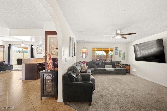 living area with light tile patterned floors, baseboards, ceiling fan, a textured ceiling, and light colored carpet