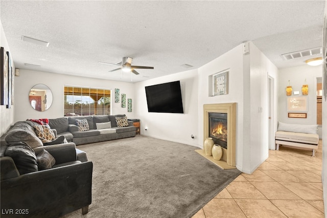 living room with light tile patterned floors, visible vents, a textured ceiling, a glass covered fireplace, and light carpet