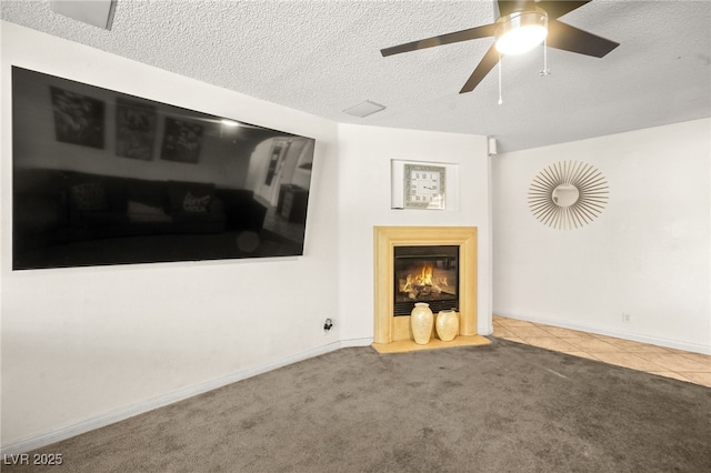 unfurnished living room featuring tile patterned floors, a textured ceiling, a glass covered fireplace, carpet, and baseboards