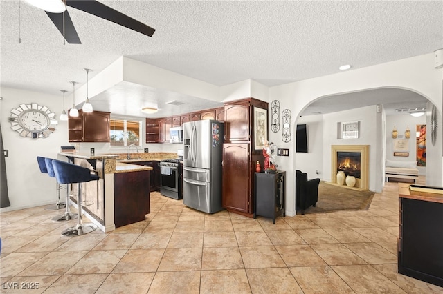 kitchen featuring a peninsula, a warm lit fireplace, a sink, appliances with stainless steel finishes, and a kitchen breakfast bar