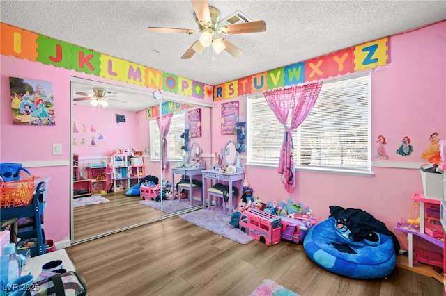 playroom with ceiling fan, wood finished floors, visible vents, and a textured ceiling