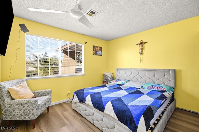 bedroom with visible vents, baseboards, wood finished floors, a textured ceiling, and a ceiling fan