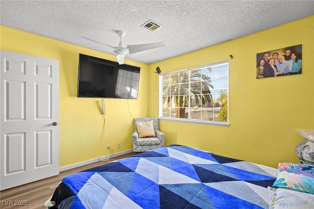 bedroom featuring visible vents, a ceiling fan, a textured ceiling, wood finished floors, and baseboards