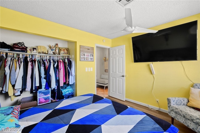 bedroom with wood finished floors, baseboards, visible vents, a closet, and a textured ceiling