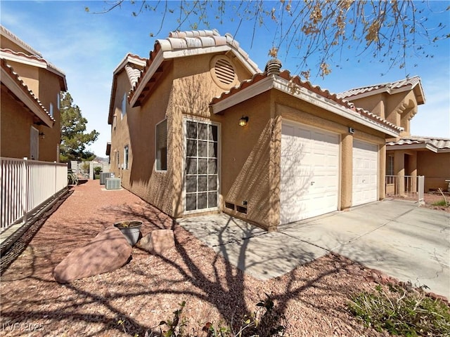 view of side of property with fence, a tile roof, concrete driveway, stucco siding, and cooling unit