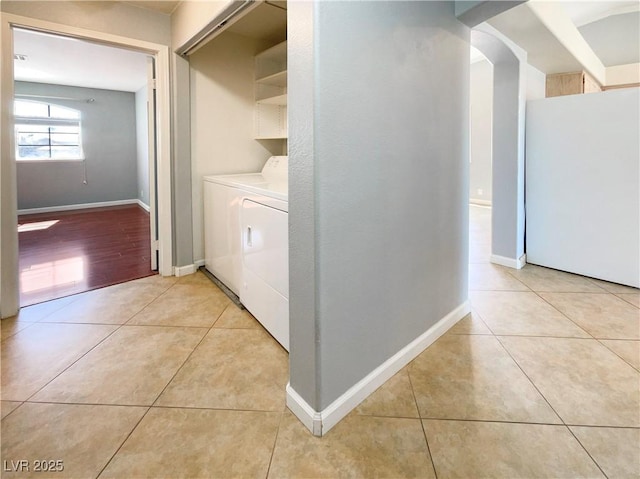 washroom with baseboards, washing machine and clothes dryer, laundry area, light tile patterned flooring, and arched walkways