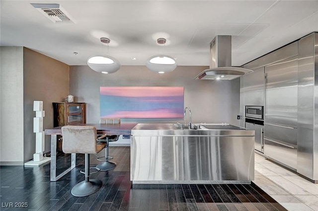 kitchen with visible vents, island exhaust hood, stainless steel microwave, wood finished floors, and black electric cooktop