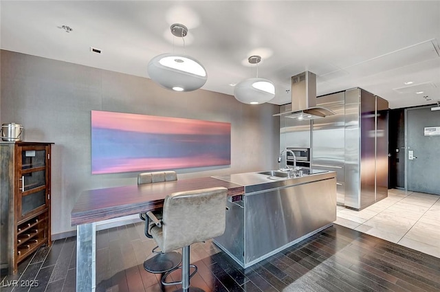 kitchen with wood finished floors, island exhaust hood, stainless steel counters, and a sink