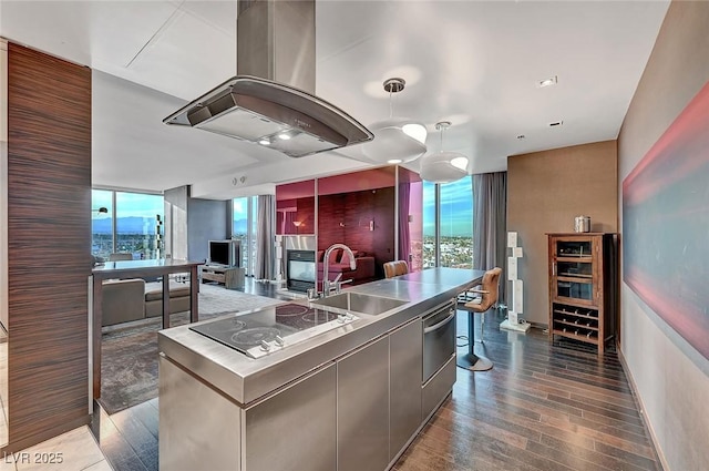 kitchen featuring a wall of windows, a sink, stainless steel counters, black electric cooktop, and island range hood