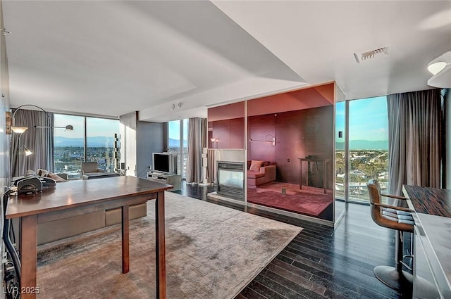 office featuring a multi sided fireplace, visible vents, dark wood-style flooring, and expansive windows