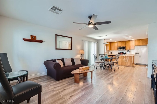 living area with visible vents, baseboards, light wood-style floors, and a ceiling fan